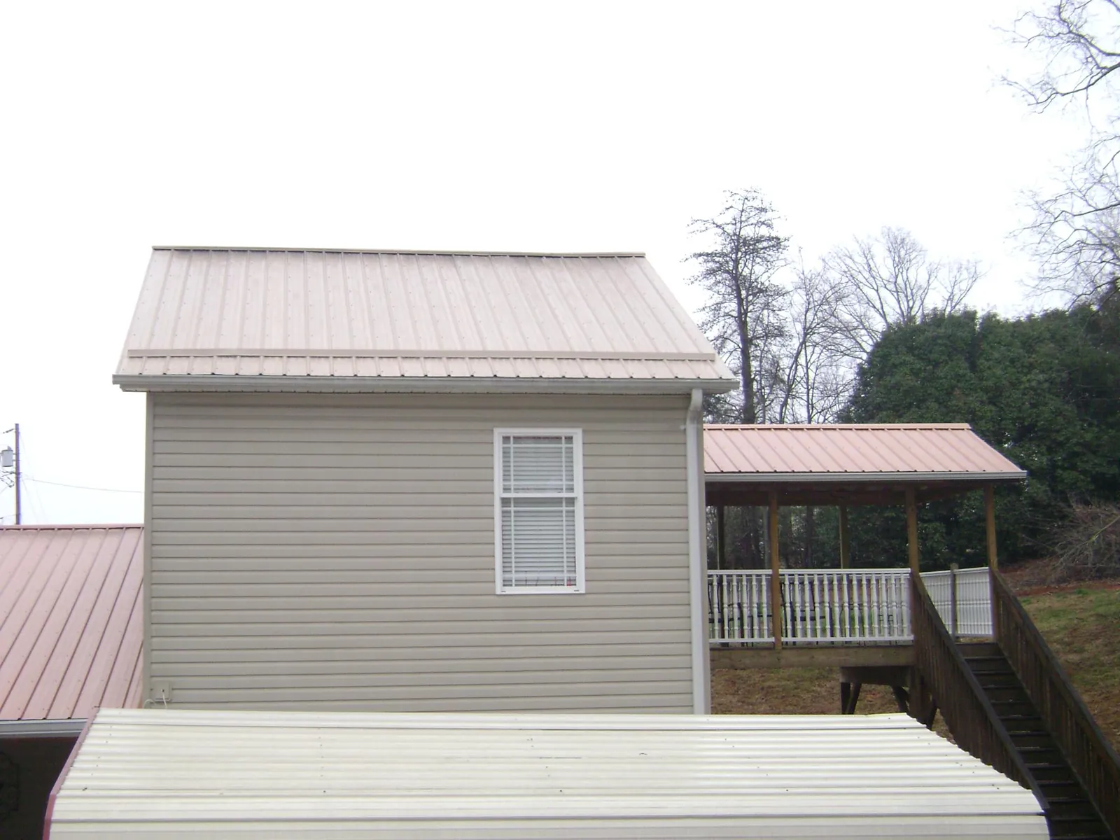 Tan metal roofs on a two story addition and attached porch, from a Roof Replacement job in Plainfield